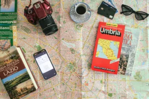 Flat lay for planning a trip to Italy: Milan city map, Umbria road map, a flight boarding pass, camera and travel guidebooks